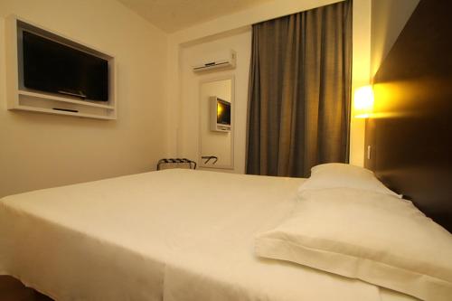 a bedroom with a white bed with a flat screen tv at Hotel Ipê MS in Campo Grande