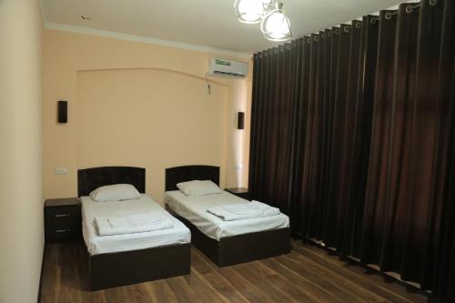 2 Betten in einem Zimmer mit schwarzen Vorhängen in der Unterkunft BUXOROYI SHARIF Hotel in Buxoro