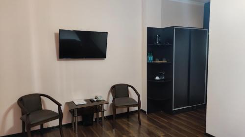2 Stühle und ein Tisch mit einem TV an der Wand in der Unterkunft BUXOROYI SHARIF Hotel in Buxoro