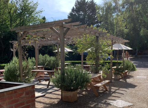 a wooden pergola with picnic tables and benches at John Barleycorn in Duxford