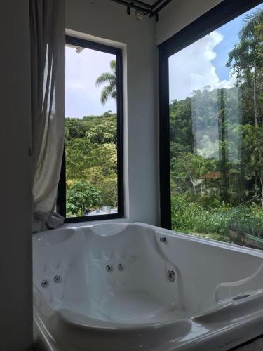 a bath tub in a bathroom with two windows at casa natureza Mariscal in Bombinhas