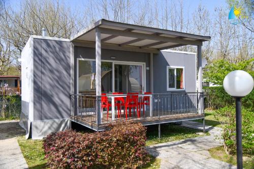 a tiny house with a deck and red chairs at Camping Rose in Dormelletto