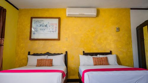 two beds in a room with a yellow wall at Hotel Mucuy in Mérida