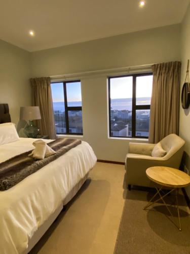 a bedroom with a bed and a chair and windows at Waves Edge CP3 in Cape Town