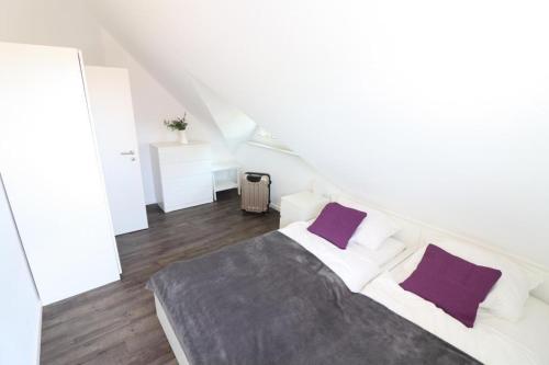 een witte slaapkamer met een groot bed met paarse kussens bij Ferienhaus-im-Angerdorf in Cuxhaven