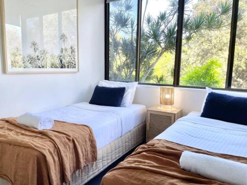two beds in a room with two windows at Surf Haven opposite Clarkes Beach pool walk to CBD in Byron Bay