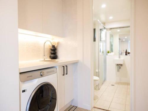 a white bathroom with a washing machine and a sink at Castaway opposite Clarkes Beach in Byron Bay