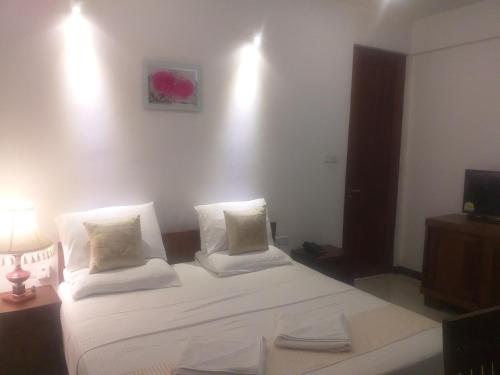 a bedroom with a bed with white sheets and a television at De Mansion Hotels in Katugastota