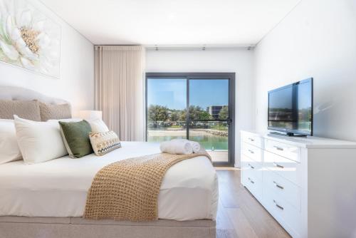 a white bedroom with a large bed and a tv at Maraboo Island Beachfront Villa in Fremantle