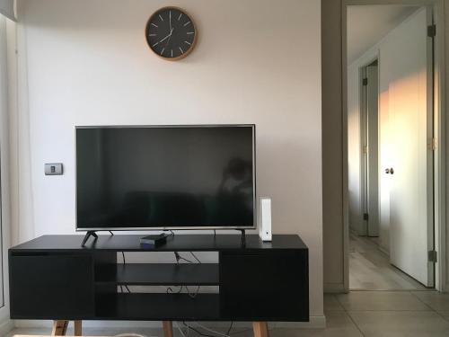 a television on a black entertainment center with a clock on a wall at Elegante y acogedor departamento con gran vista, cercano a todo in Concepción