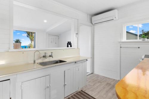 a white kitchen with a sink and two windows at Karitane Cottage - Karitane Holiday Home in Karitane