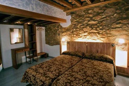 1 dormitorio con cama y pared de piedra en EL Molino de Tormellas exclusivo alojamiento rural en un antiguo molino, en Tormellas