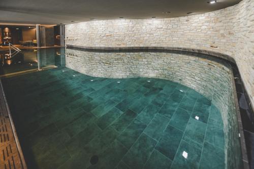 una piscina con pared de ladrillo y suelo verde en Arabella Retreat & Spa, en Nauders