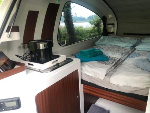 a bedroom with a bed and a window in an rv at Sealander - Tiny Wohnwagen und Boot - Ferienwohnung Creutzig am Campingplatz Schachenhorn in Bodman-Ludwigshafen