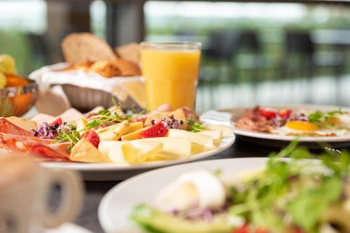 a table with plates of food and a glass of orange juice at Hotel Helikon, Keszthely in Keszthely