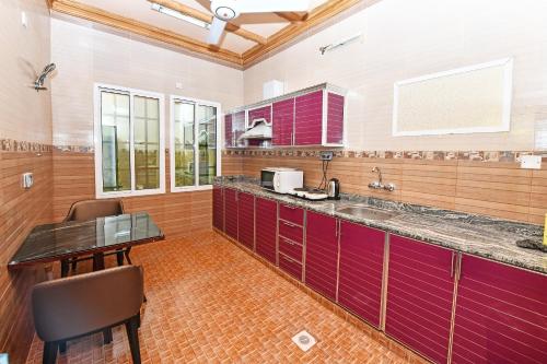 eine große Küche mit roten Schränken und einem Tisch in der Unterkunft OYO 139 Al Ghadeer Hotel Apartments in Barka
