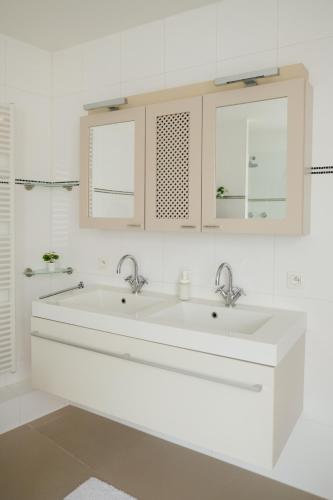 a white bathroom with two sinks and two windows at In De Witte Engel in Lanaken