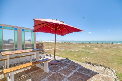 a red umbrella sitting on a bench next to the beach at Colours of the Sea Apartment in Struisbaai