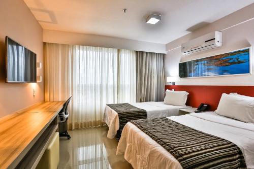 a hotel room with two beds and a tv at Ramada Hotel & Suites Campos Pelinca in Campos dos Goytacazes