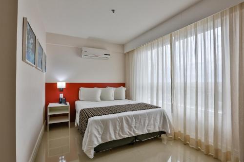a bedroom with a bed and a large window at Ramada Hotel & Suites Campos Pelinca in Campos dos Goytacazes