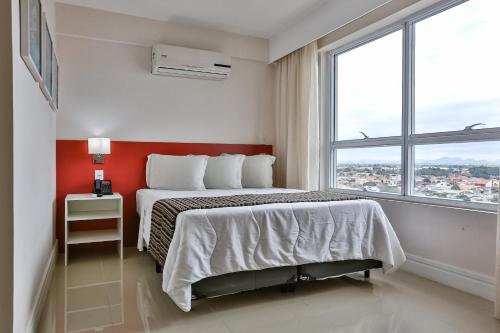 a bedroom with a bed and a large window at Ramada Hotel & Suites Campos Pelinca in Campos dos Goytacazes