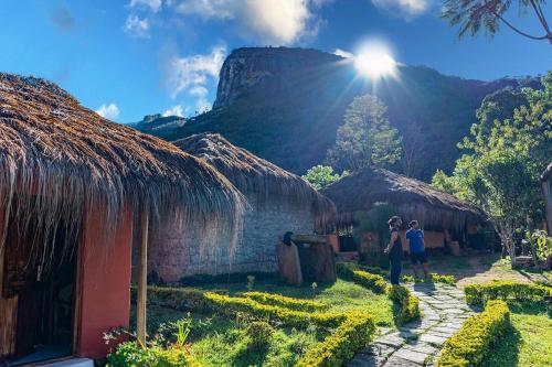 two people standing in front of a house with a mountain in the background at Deshadan Eco Valley Resort - An Eco friendly Mud House in Kanthalloor