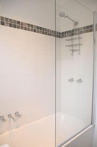 a shower with a glass door next to a tub at Bush & Bay Cottage in Erowal Bay