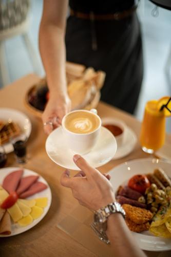 a person holding a cup of coffee on a table with food at Millennium Place Mirdif in Dubai