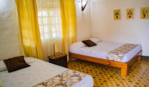 two beds in a room with yellow curtains at Hotel La Coqueta in Montenegro