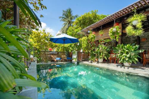a swimming pool with an umbrella next to a house at Sands River Hoi An Villa in Hoi An
