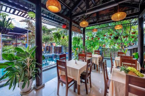 a restaurant with tables and chairs and plants at Sands River Hoi An Villa in Hoi An