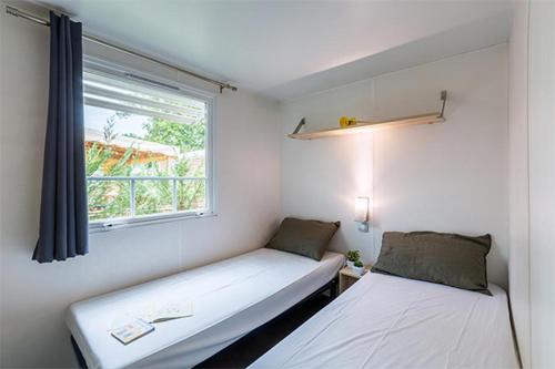 ein kleines Zimmer mit 2 Betten und einem Fenster in der Unterkunft CAMPING LA PINEDE in Les Mathes