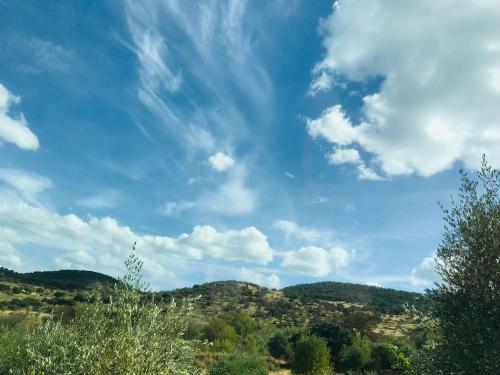 een blauwe lucht met wolken boven heuvels en bomen bij Casa Bibiana in Posadilla