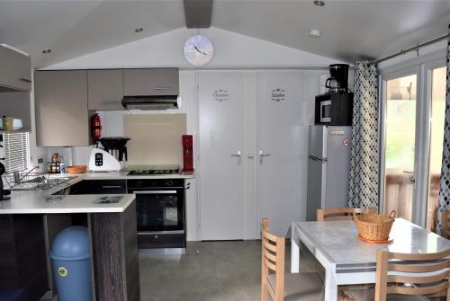 une cuisine avec des placards blancs, une table et une horloge dans l'établissement Spacieux Mobil-home N°502 - 2 chambres - dans Camping 4 *, à Gastes