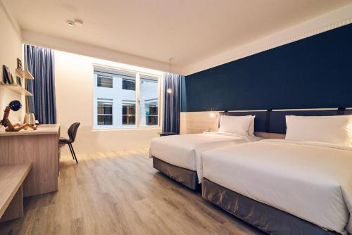 台北市にあるCHECK inn Select Taipei Nangangのベッド2台、デスク、窓が備わるホテルルームです。