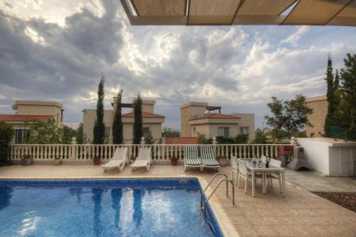 a swimming pool with chairs and a table on a patio at Villa Athina in Paphos