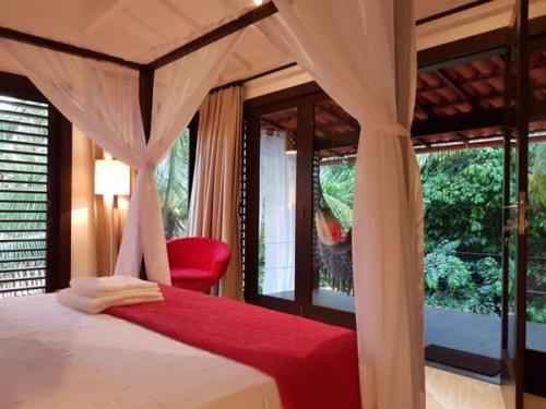 um quarto com uma cama de dossel e uma cadeira vermelha em Mangueira Boutique Hotel Moreré na Ilha de Boipeba