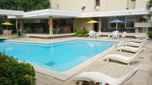 a swimming pool with white chairs and tables next to a building at Vallclaire Suites in Barranquilla