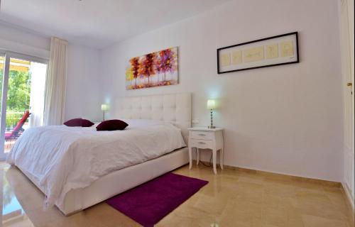 ベナルマデナにあるPalmeras del Golfの白いベッドと紫色のラグが備わる白いベッドルーム1室が備わります。