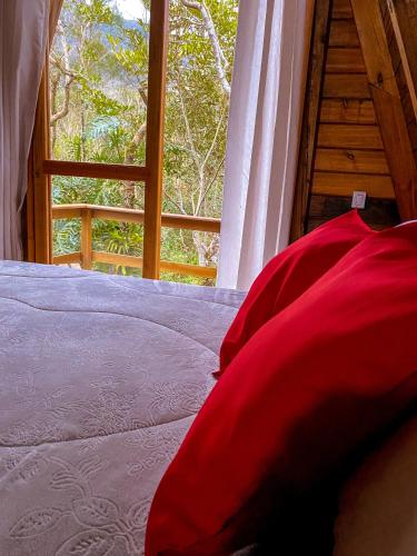 a bed with red pillows in front of a window at Morada do Corujão - Sossego das Águas in Praia Grande