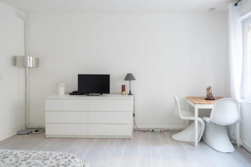 a white bedroom with a desk and a tv on a dresser at Spacious studio in the center of Montmartre in Paris