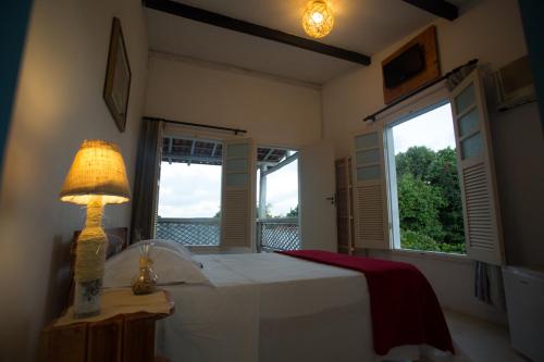 um quarto com uma cama com um candeeiro e 2 janelas em Pousada Vila Mundi Itaúnas em Itaúnas