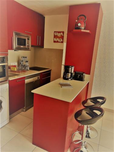 une cuisine avec des placards rouges et deux tabourets de bar dans l'établissement Hikoa Hendaia-Hendaye plage, à Hendaye