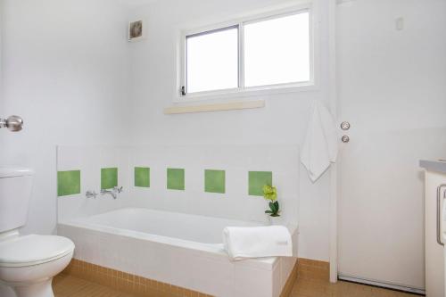 a white bathroom with a tub and a toilet at Beach Retreat in Mollymook