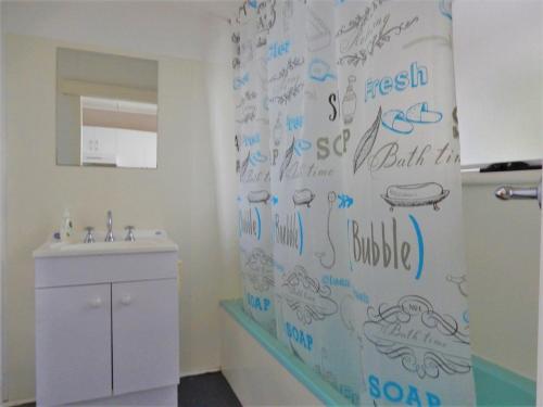 a bathroom with a shower curtain with writing on the wall at Donlan's Beach Cottage in Mollymook
