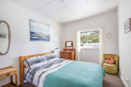 a bedroom with a bed and a chair and a window at Retro Beach Cottage in Kioloa