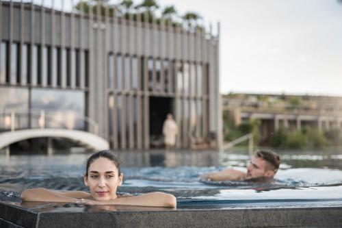 a man and woman swimming in a swimming pool at ADLER Spa Resort SICILIA in Siculiana