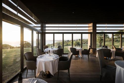 un restaurante con mesas, sillas y ventanas grandes en ADLER Spa Resort SICILIA en Siculiana