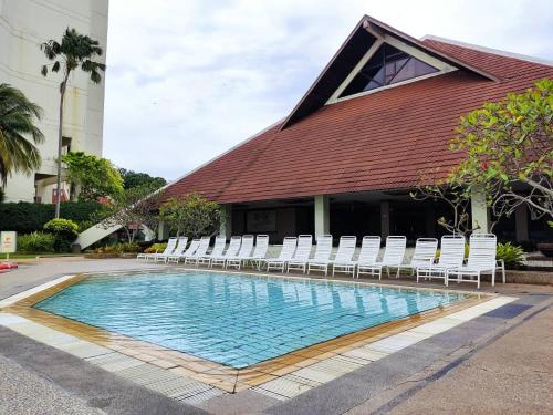 ein Pool mit weißen Stühlen und ein Gebäude in der Unterkunft Tanjung tuan regency private PD in Port Dickson