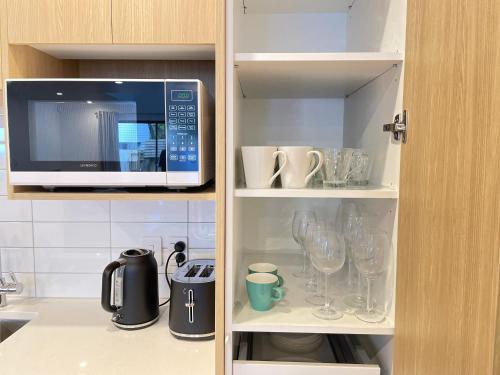 a microwave in a kitchen with wine glasses at NO PARTY ALLOWED, Entire Brand New 3 bedroom townhouse, free unlimited fibre wifi and free parking in Wellington
